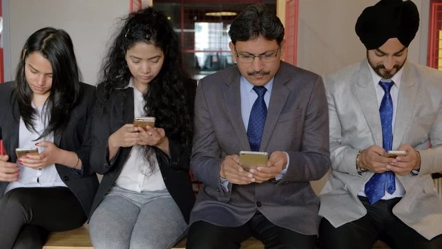 Team in business formals jus wasting time while being addicted and looking only at their phone screens and ignoring each other, young and old, males and females 
