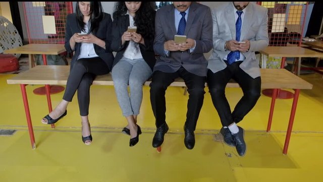 Tilt down to up to colleagues in business formals jus wasting time while being addicted and looking only at phone screens and ignoring each other, young and old, males and females at a coworking space