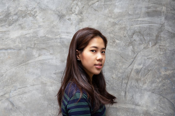 Portrait of teenager woman standing on grey concrete wall looking at camera.