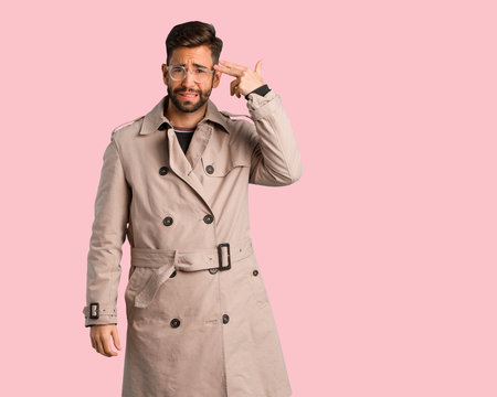 Young man wearing trench coat doing a suicide gesture