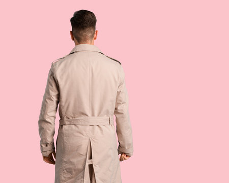 Young man wearing trench coat from behind, looking back