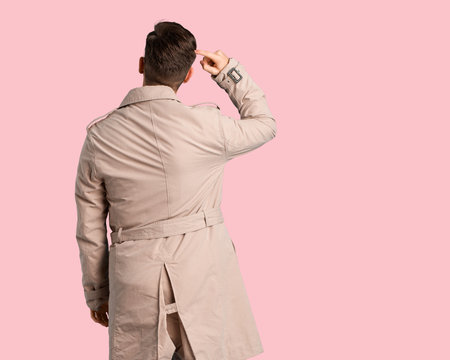 Young man wearing trench coat from behind thinking about something