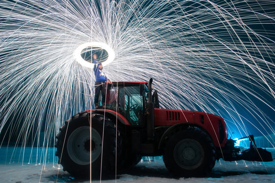 Man sparks on the background of a red tractor, steel wool photo, sparks on a long exposure,