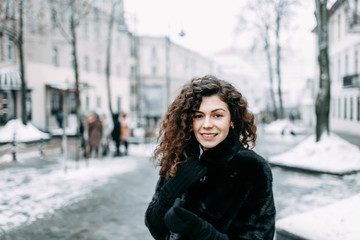 beautiful curly brunette girl in a fur black coat walks through the winter city.