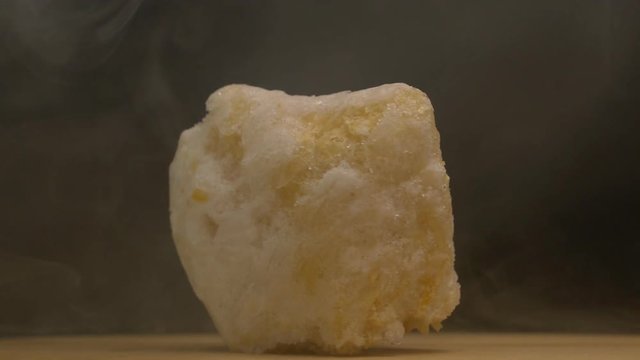 A piece of rotating frozen pumpkin on a black background, from which emanates cold and evaporation, close-up, slow mo