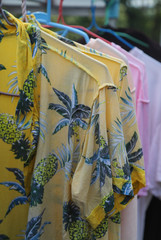 Closeup of yellow shirt and others hanging on hangers for drying under sunlight. The way of energy saving for global warming reduction. Vertical view. 