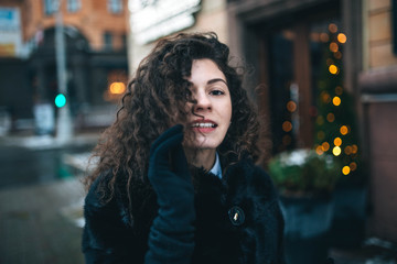 beautiful curly brunette girl in a fur black coat walks through the winter city.