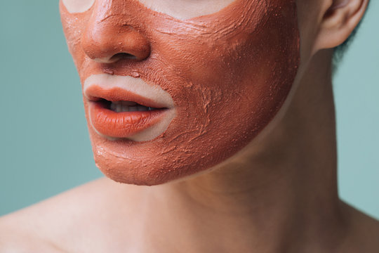 Unrecognisable cropped woman posing with orange lipstick and cosmetic face mask on her face.