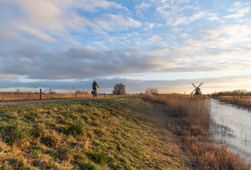 Woman cycling in the Dutch countryside near a traditional windmill. Groningen, the Netherlands.