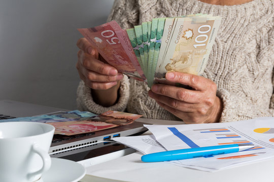 Money from Canada: Canadian Dollars. Senior person handling bill on desk.