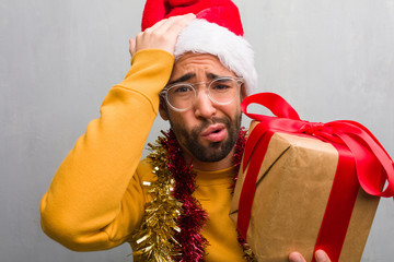 Young man sitting with gifts celebrating christmas worried and overwhelmed