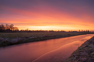 Colourful, winter sunrise over a small canal in the Dutch countryside. Groningen province, Holland.