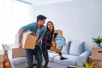 Home, people, moving and real estate concept - happy couple having fun in cardboard boxes at new home.