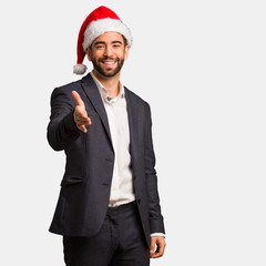 Young business man wearing santa hat reaching out to greet someone