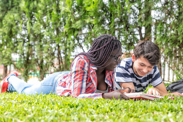 Couple of friends laying down on the grass with school lesson