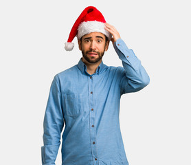 Young man wearing santa hat worried and overwhelmed