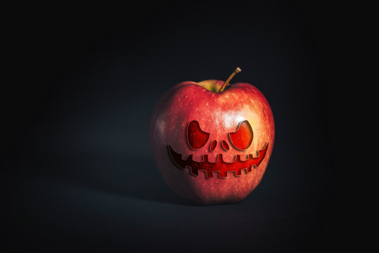 A red ripe Apple on a black background with a frightening helluin face.