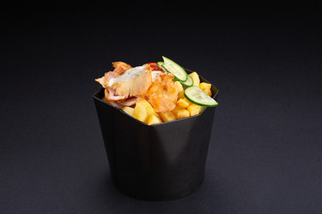 Chicken slices with French fries and vegetables on a black background.