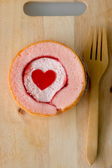 Cake roll with strawberry marmalade jam and jelly shape heart on wood with wood fork.