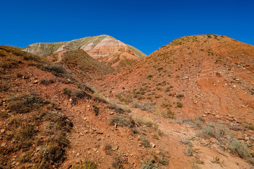 Red Mountain Big Bogdo on a background of blue sky. In the cliffs of the eastern slopes to the surface of the most ancient layers of terrestrial rocks