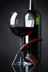 Red wine with corkscrew on a black background.
