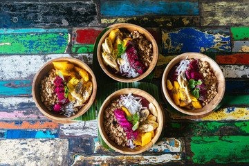 Close up four smoothies bowls made with mango, banana, granola, grated coconut, dragon fruit, chia seeds and mint on colored background