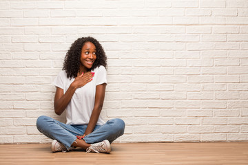 Young black woman sitting on a wooden floor doing a romantic gesture, in love with someone or showing affection for some friend