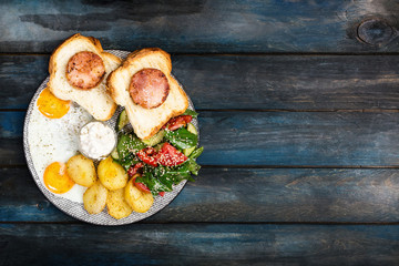Big delicious breakfast with fried eggs, fried potatoes, fresh salad, chicken ham on bread and cream sauce. Top view, copy space for your text