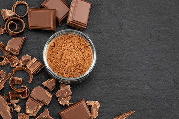 Broken chocolate pieces and cocoa powder on a dark background. Top view with copyspace for your text