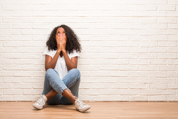 Young black woman sitting on a wooden floor very scared and afraid, desperate for something, cries of suffering and open eyes, concept of madness