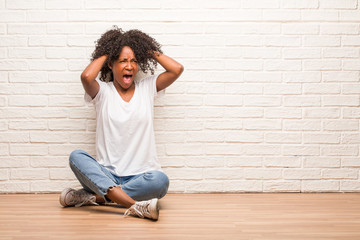 Young black woman sitting on wooden floor crazy and desperate, screaming out of control, funny lunatic expressing freedom and wild