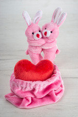 Pink toy bunnies hugging near pink bag with love heart