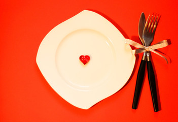 White asymmetrical plate, white red heart on it. Knife and fork with silver ribbon, red background. Perfect for Valentine's, anniversary, wedding, romantic event