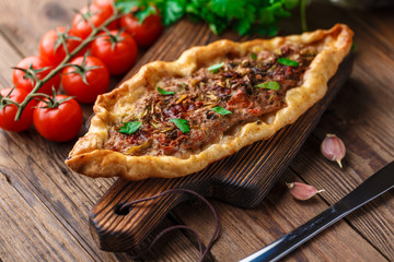 Turkish handmade pide lies on an old brown wooden table. Cherry tomatoes, parsley, lemon, hot pepper, garlic are on the table.
