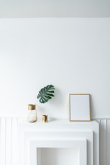 Composition of empty gold frame & artificial plant in glass vase with gold stainless trim edge and gold mirror vase setting on empty  fireplace in minimal modern style /empty space fo advrtisement