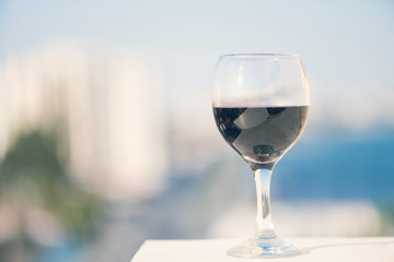 Close up of glass of red wine against the background of blurred town with bokeh at summer evening
