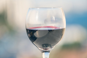 Close up of glass of red wine against the background of blurred town with bokeh at summer evening