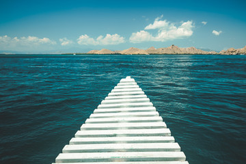 Close-up white pier leading to the ocean. Komodo island, Indonesia. Amazing marine scene. The cloudy sky over the crystal clear water. The romantic road into the distance. The conceptual image.