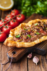 Turkish handmade pide lies on an old brown wooden table. Cherry tomatoes, parsley, lemon, hot pepper, garlic are on the table.