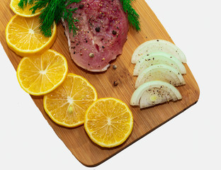 Fresh raw pork meat with spices, lemon and onion on wooden cutting board 