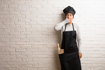 Young baker indian woman against a bricks wall covering mouth, symbol of silence and repression, trying not to say anything