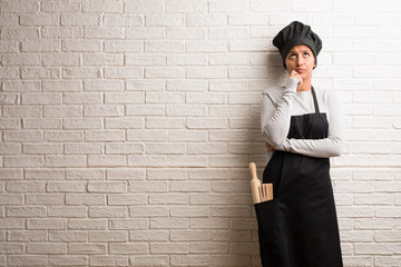 Young baker indian woman against a bricks wall doubting and confused, thinking of an idea or worried about something