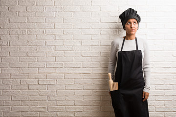 Young baker indian woman against a bricks wall doubting and confused, thinking of an idea or worried about something