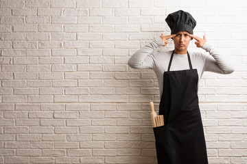 Young baker indian woman against a bricks wall man making a concentration gesture, looking straight ahead focused on a goal