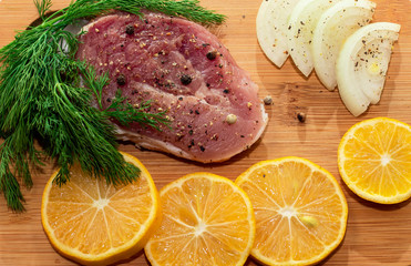 Fresh raw pork meat with spices, lemon and onion on wooden cutting board 
