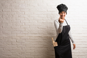 Young baker indian woman against a bricks wall inviting to come, confident and smiling making a gesture with hand, being positive and friendly