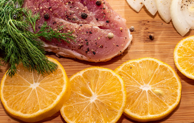 Fresh raw pork meat with spices, lemon and onion on wooden cutting board 