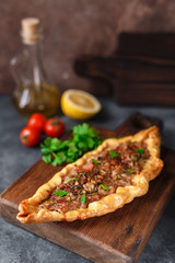 Turkish handmade pide lies on an blue surface. Cherry tomatoes, parsley, lemon, hot pepper, garlic are on the table.