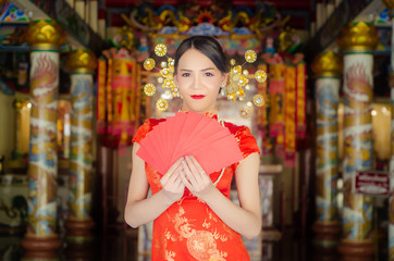 Fototapeta na wymiar happy Chinese new year. Asian girl with gesture of congratulation and holding red envelope on Chinese temple background.