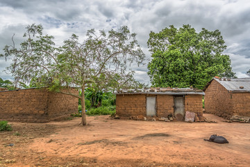 Fototapeta na wymiar View of traditional village, a coat resting outdoor and zinc sheet on roof houses and terracotta brick walls, cloudy sky as background
